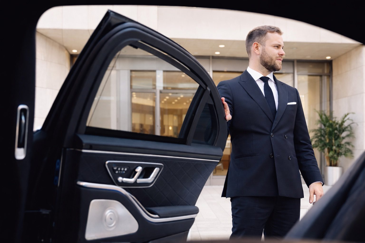 Chauffeur im dunklen Anzug hält die hintere Tür einer Limousine auf