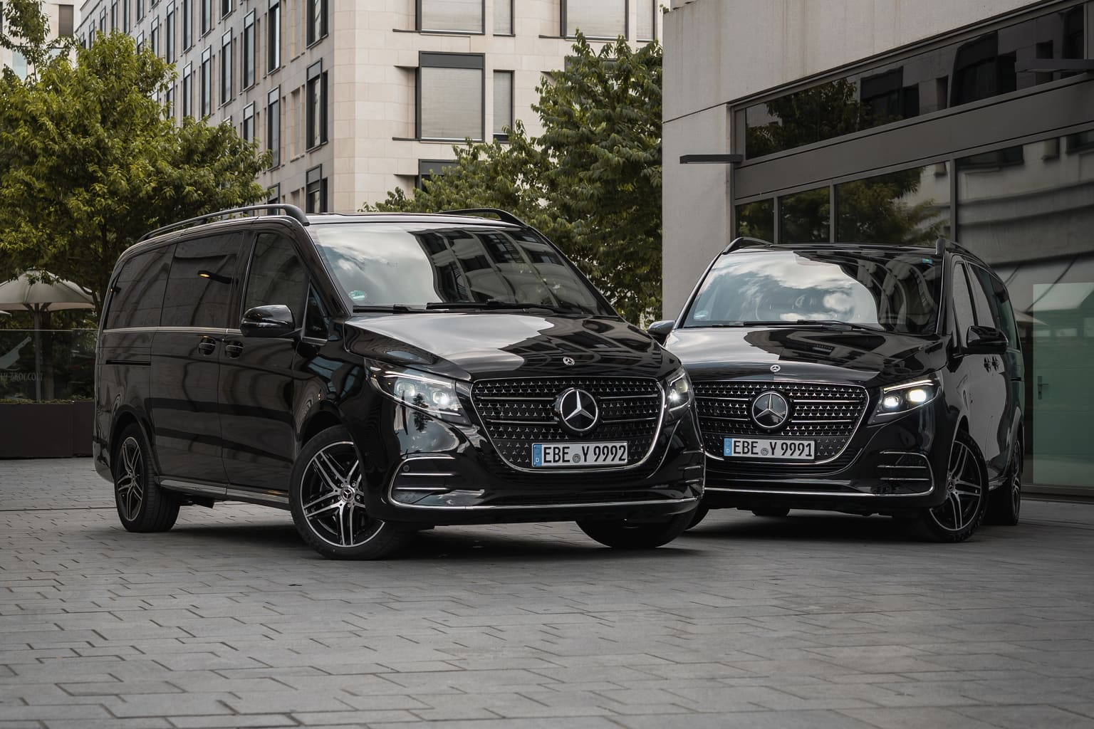 Zwei schwarze Mercedes-Benz V-Klassen von AYDEN nebeneinander in einem Innenhof zwischen Bürogebäuden