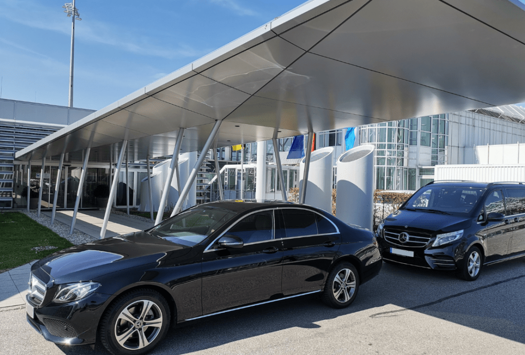 Zwei luxuriöse schwarze Fahrzeuge von Ayden, geparkt vor einem modernen Terminal am Flughafen München, bieten eine exklusive Taxi-Alternative.