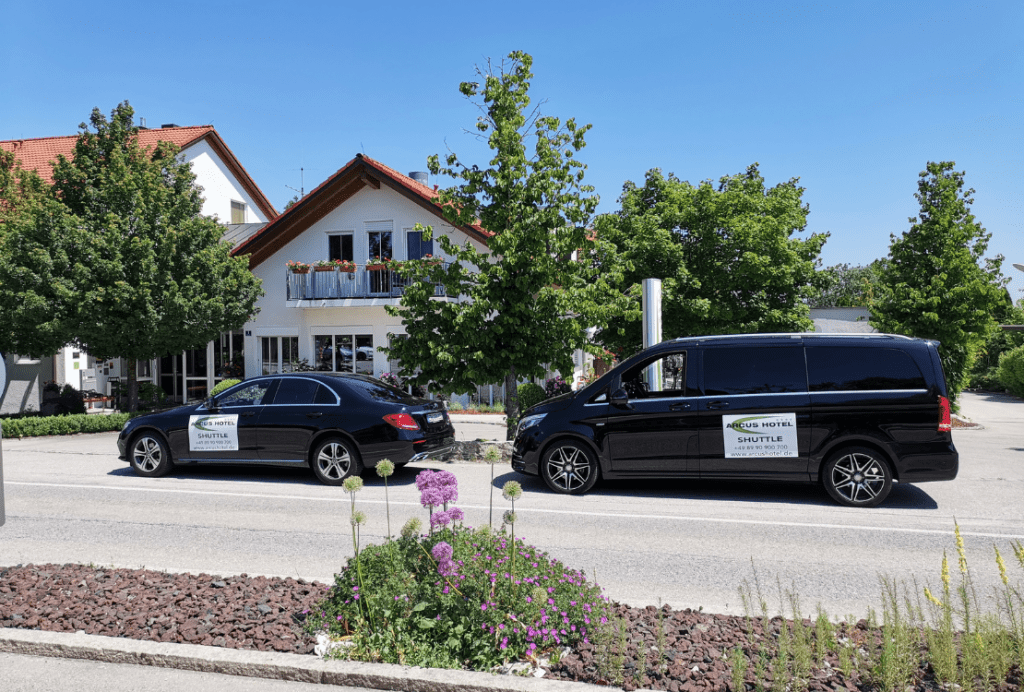 Zwei luxuriöse schwarze Fahrzeuge von Ayden, geparkt vor dem Arcus Hotel in Vaterstetten, bieten eine exklusive Taxi-Alternative.